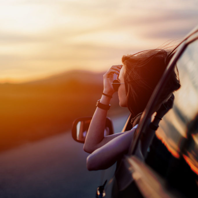 Beauty in time of sunset Beautiful young woman sitting in the car on the country road and looking at the view on a beautiful sunny spring day